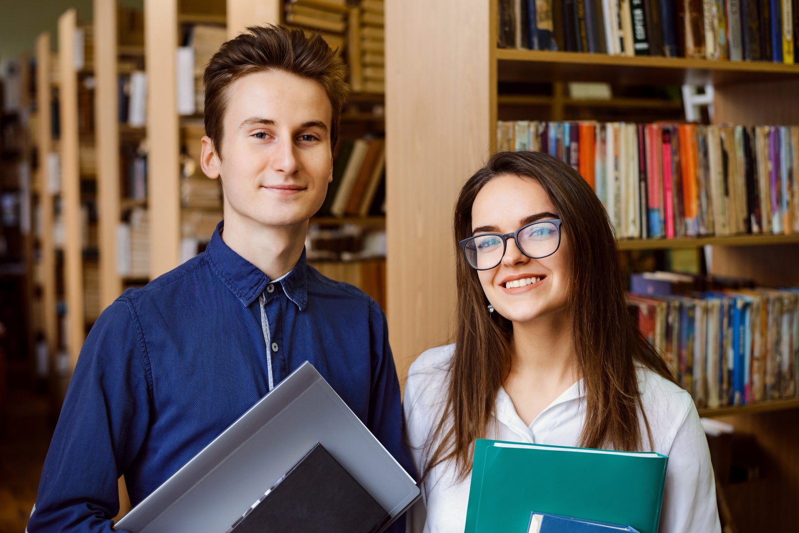 Young college students at the library in front of shelves of books, studying together, smiling to the camera, eager to study